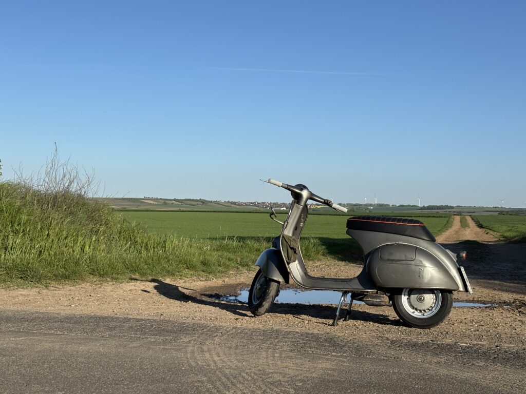 Bild einer grauen Vespa mit Rheinhessischer Landschaft im Hintergrund.